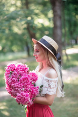 Young beautiful woman in straw hat holding flowers. Pretty girl with peony pink. Beauty portrait