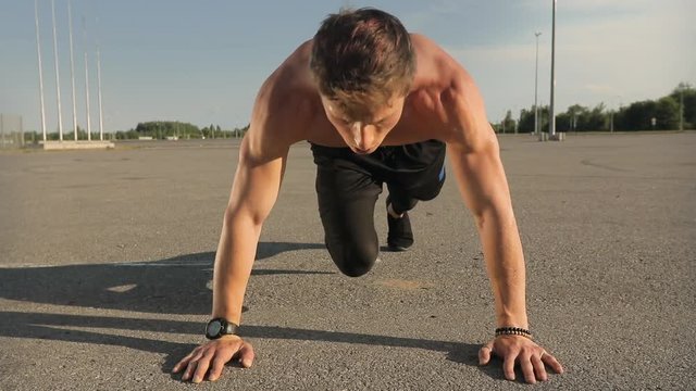 Young athletic man making sports exercises outdoors, maintaining muscular posture