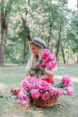 woman florist in straw hat makes a bouquet with pink peonies flowers in park