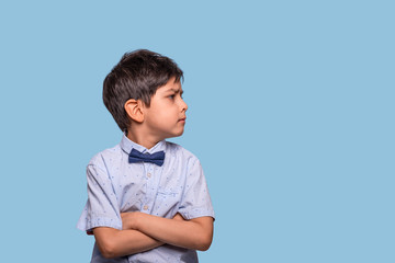 Studio shot of a serious   boy wearing   blue  shirt with bow against   blue background with copy space.