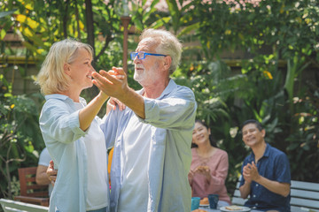 Happy senior couple dancing after breakfast in the morning with their family at home garden