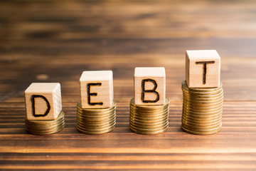 inscription debt wooden cubes with letters, money piles of coins,  wooden background