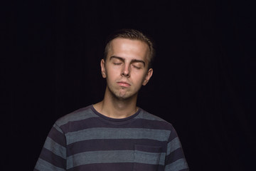 Close up portrait of young man isolated on black studio background. Photoshot of real emotions of male model with closed eyes. Thoughtful. Facial expression, human nature and emotions concept.