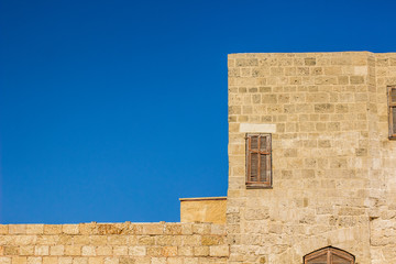 medieval building ancient stone wall with closed wooden shutters window corner frame geometric shape background wallpaper pattern concept photography with empty blue sky and space for copy or text 