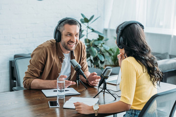 cheerful radio host talking to colleague while sitting at workplace in studio