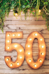 Beautiful wooden photozone with the inscription 50 decorated with natural greenery and a garland.
