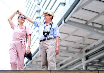 Couple of Asian old man and woman tourist are dancing among the big building of big city. This photo also contain concept of good life of elderly people.