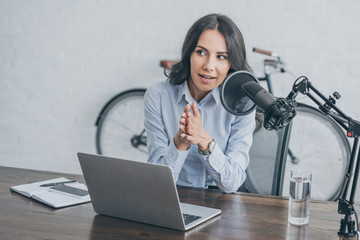 pretty radio host speaking in microphone while sitting at desk near laptop