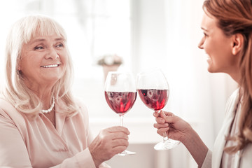 Dark-haired smiling woman having a glass of wine with her mother