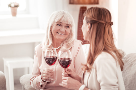 Blond elderly smiling woman having a glass of wine with her daughter