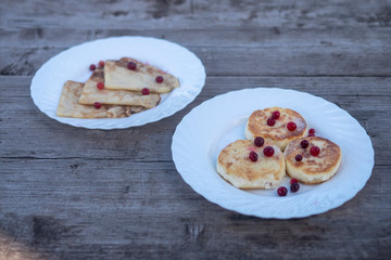 pancakes with wild berries on a white plate on a wooden background