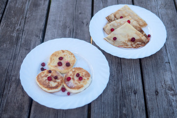 pancakes with wild berries on a white plate on a wooden background