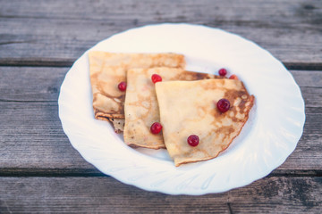 pancakes with wild berries on a white plate on a wooden background