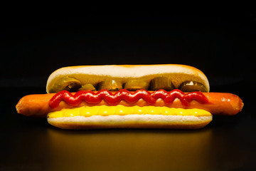 Mouthwatering long frankfurter  in a wheat bun with chili pepper rings, ketchup and cheese sauce - a classic American street food. Black background. Close-up.