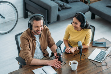 two cheerful radio hosts talking while sitting at workplace in broadcasting studio
