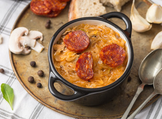 Slovak Christmas national cabbage soup in small black pot with sausage on the tablecloth background.