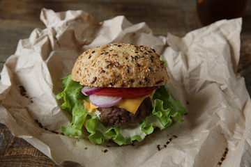 Close-up Big sandwich isolated- hamburger with beef, tomatoes, onions, cheese, lettuce and a sesame bun with coca-cola in a glass on a paper on a wooden rustic board. Fast food dinner concept.