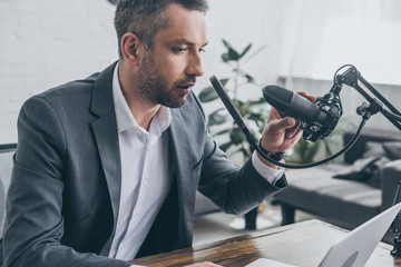 serious radio host adjusting microphone while sitting at workplace in broadcasting studio