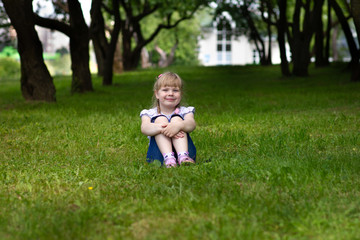 Sweet, happy little girl sitting on a grass in a park