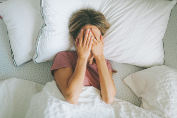 A tired woman in bed covering her face.