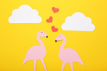 Pink paper flamingos, hearts and clouds on yellow background. Minimalism concept