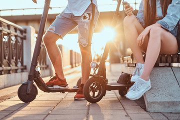 Couple of teenagers are chilling with their own electro scooters at bright sunny day.