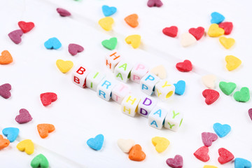 Text Happy Birthday by plastic cubes with sprinkles in shape of heart on white background