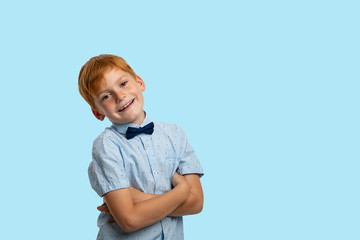 Studio shot of a smiling redhead  boy wearing   blue  shirt with bow against   blue background with copy space