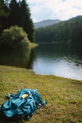 Hiking backpack lying on the grass on the lake shoreline