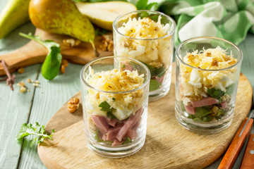 Salad with Pear, Ham, Egg, Walnuts, Fruits and Arugula on rustic wooden table.