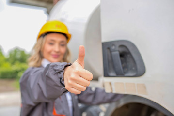 Woman, truck driver, with thumb up, standing in front of the concrete mixer truck