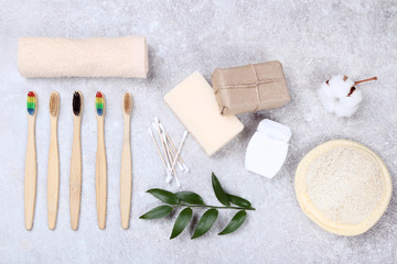 Bamboo toothbrushes with washcloth, soap, green leafs and towel on grey background