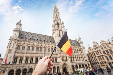 Woman tourist holds in her hand a flag of Belgium against the background of the Grand-Place Square in Brussels, Belgium