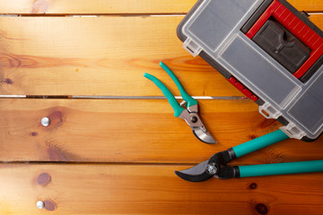 Two pairs of pruning scissors and a tool box are laying on a wooden surface
