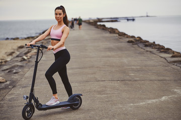 Beautiful young woman is posing for photographer at seaside with her electrical scooter.