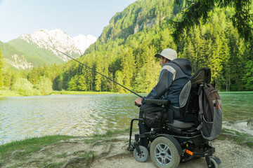 young man in a wheelchair fishing at the beautiful lake on a sunny day, with mountains in the back