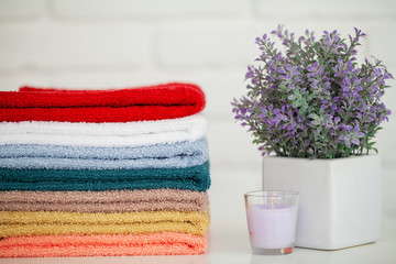 Fluffy bath towels on light wooden table with candle and white background