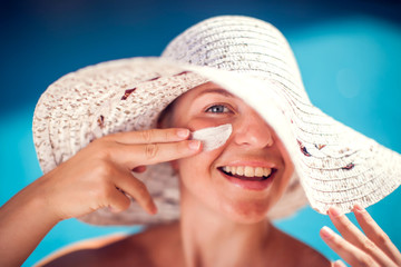 Woman with sun protection cream on her face sitting on the pool. People, summer, holiday and...