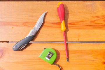 A knife, a screwdriver, and a measuring tape are laying on a brown surface
