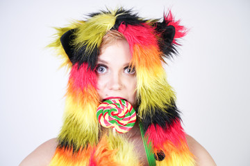 charming plus size young woman in fur hat made of multicolored fibers with cat ears and paws posing in green suspenders, black bra and funny short rainbow skirt on a white background in the Studio