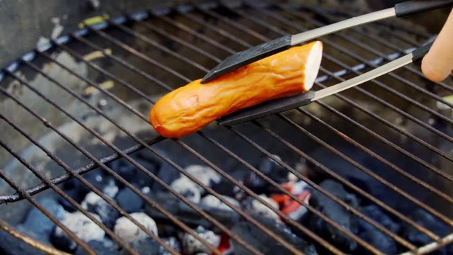 Juicy sausage on hot grill during summer barbecue in slow motion