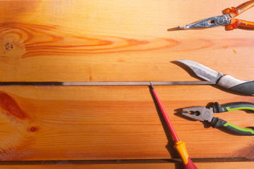 A pocket knife, screwdriver, and a hammer are laying on a wooden surface