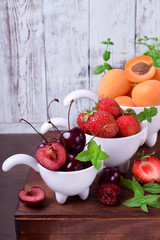 Cherries, strawberries and apricots in little white cups on the wooden table