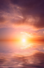 Naklejka na ściany i meble The bright orange sun rises against the backdrop of purple clouds and a calm sea.