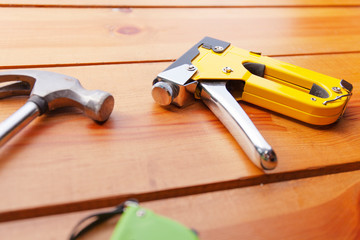 A hammer, measuring tape, and a staple gun are laying on a wooden surface