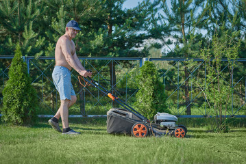 Man is using lawn mower on his countryside yard.