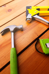 A hammer, measuring tape, and a staple gun are laying on a wooden surface