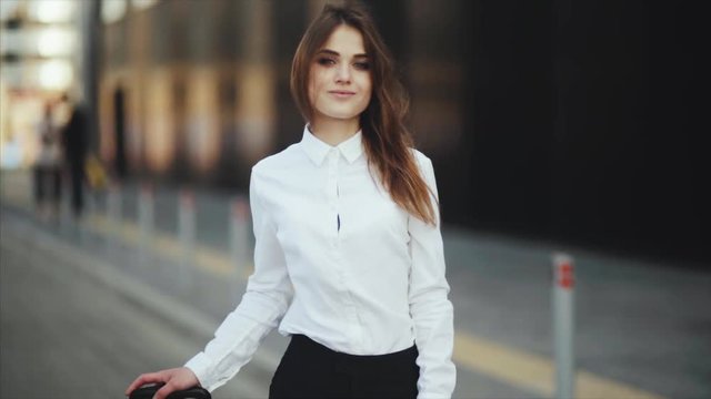Close up, slow motion. Portrait of an attractive girl with flowing black hair, she is smiling at the camera. Dressed in a white shirt and sun glasses. Style casual. Confident woman goes to a taxi or