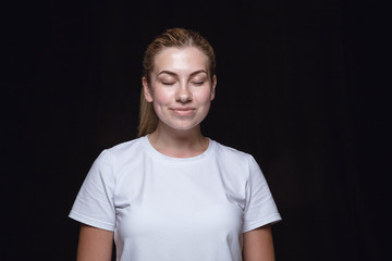 Close up portrait of young woman isolated on black studio background. Photoshot of real emotions of female model with closed eyes. Thinking and smiling. Facial expression, human emotions concept.