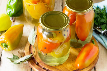 Homemade preserving. Bulgarian Pepper stuffed with vegetables in marinade on the kitchen wooden background.